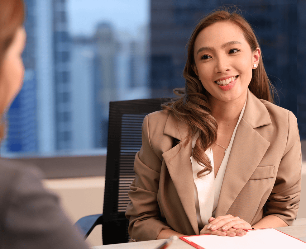 A woman seated at a desk, all smiles in what seems to be customer- client discussion